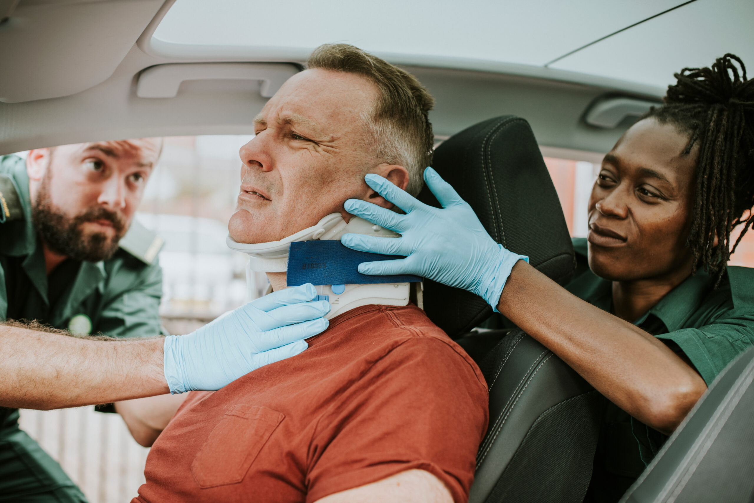 Emergency responders fitting a neck brace on an injured man seated in a car after an accident.