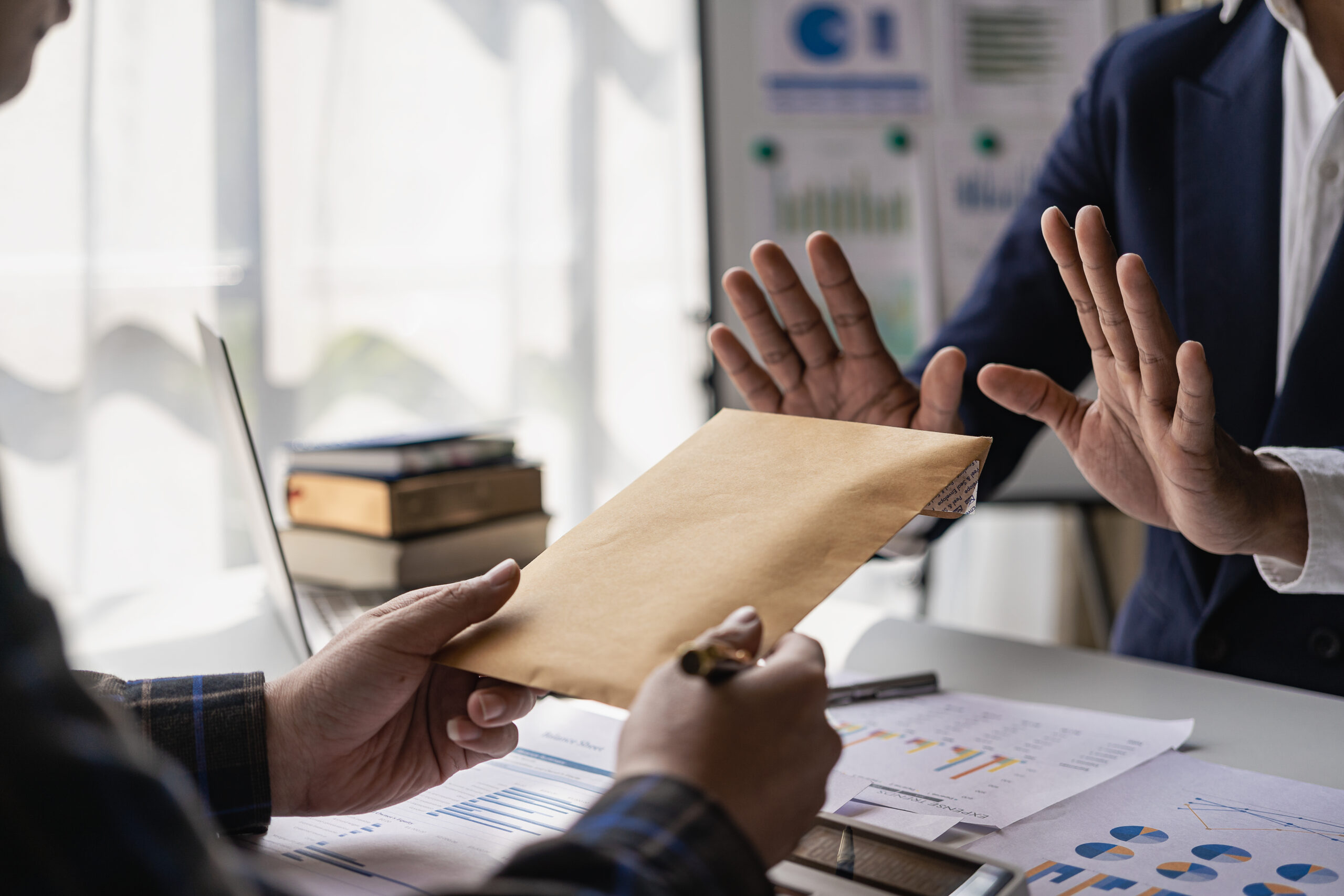 Person refusing a cash-filled envelope offered across a desk with financial documents