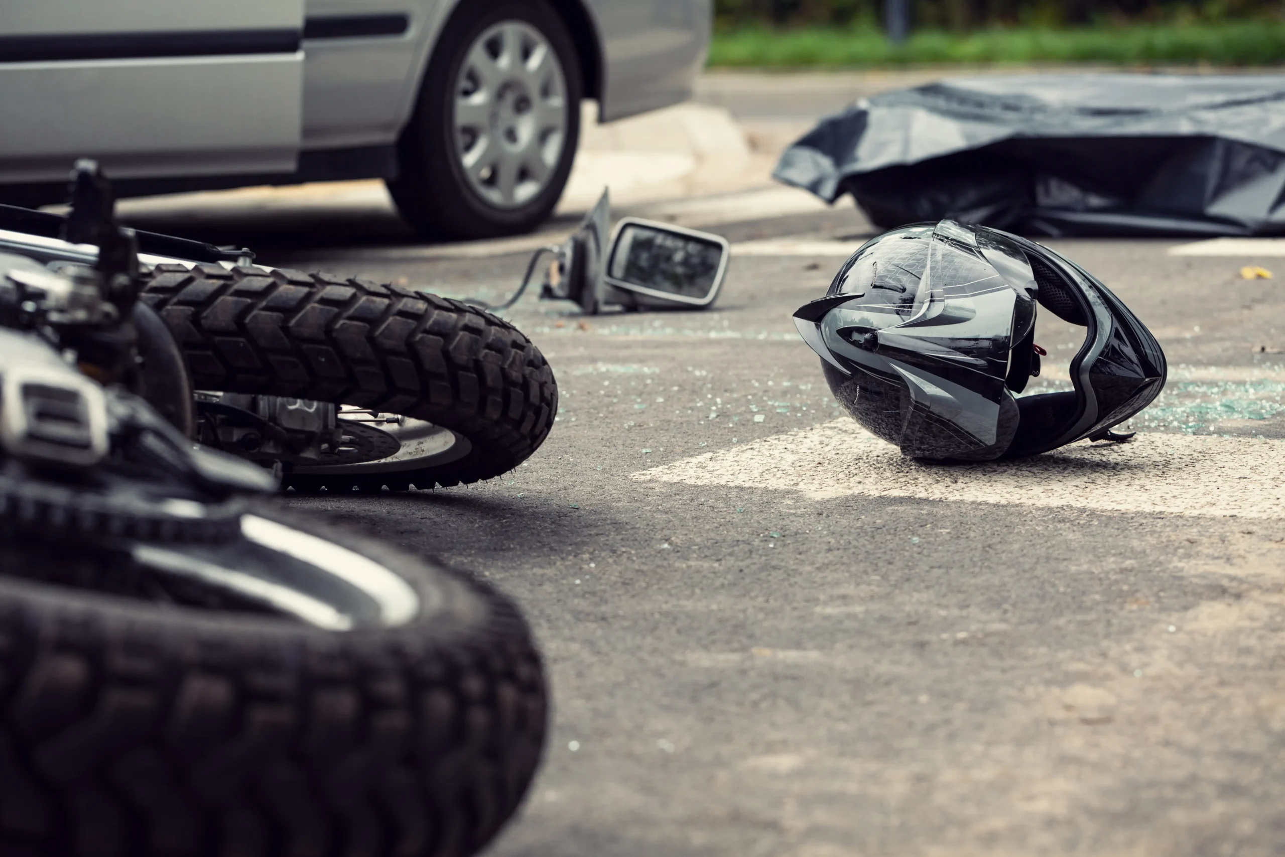 Fallen motorcycle and damaged helmet lying on the pavement beside a car after a collision