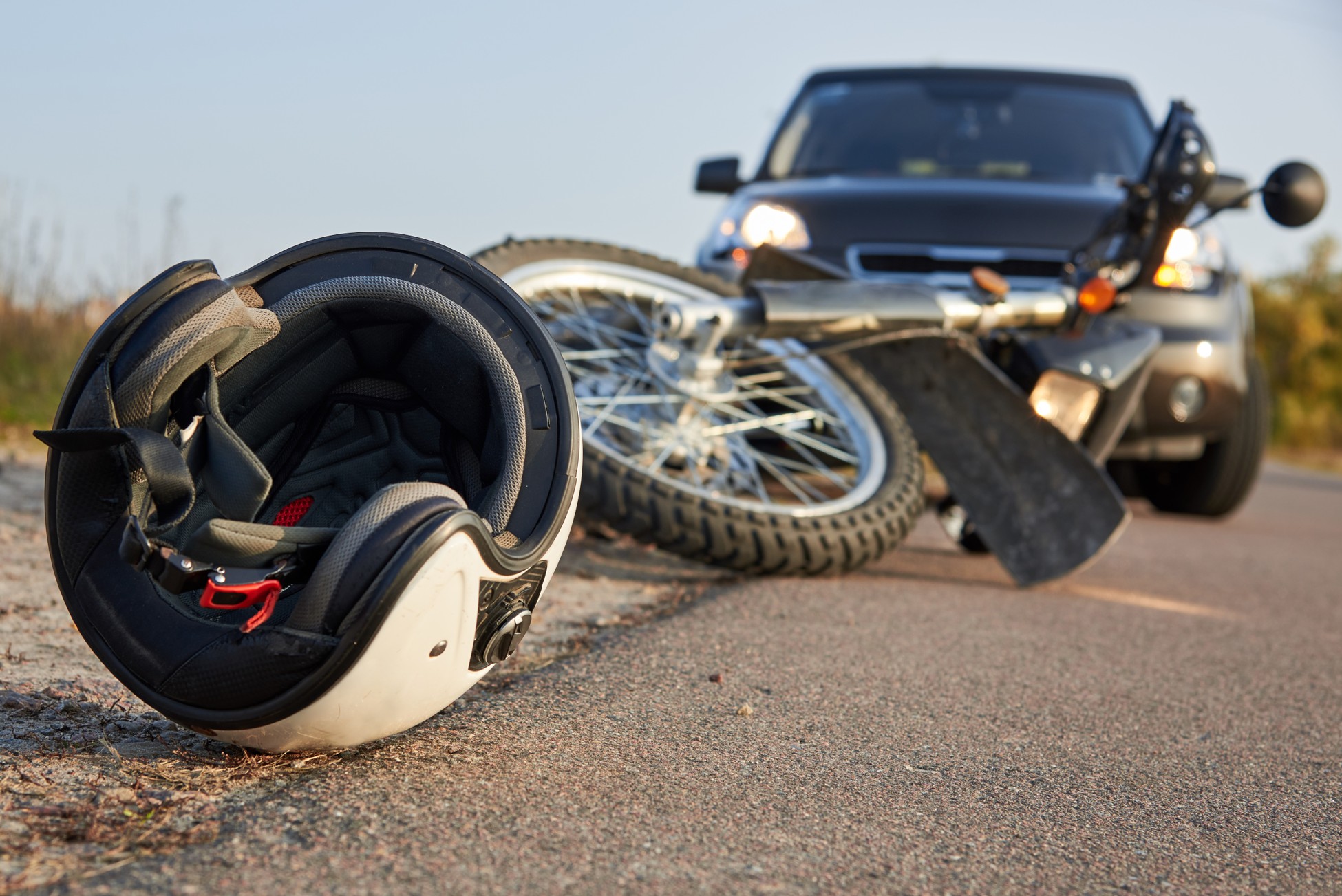 Motorcycle and rider's helmet lying on the road after a collision with a car in the background