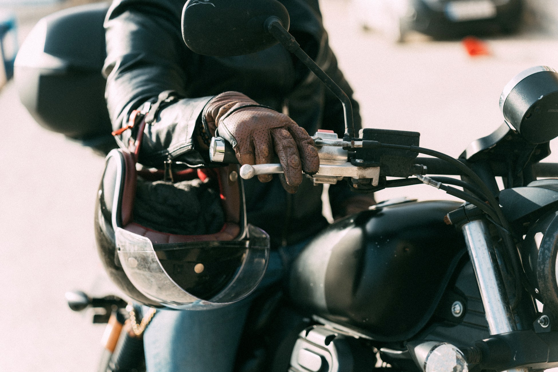 Close-up of a motorcyclist's gloved hand on the handlebars with a helmet resting on the tank before a ride