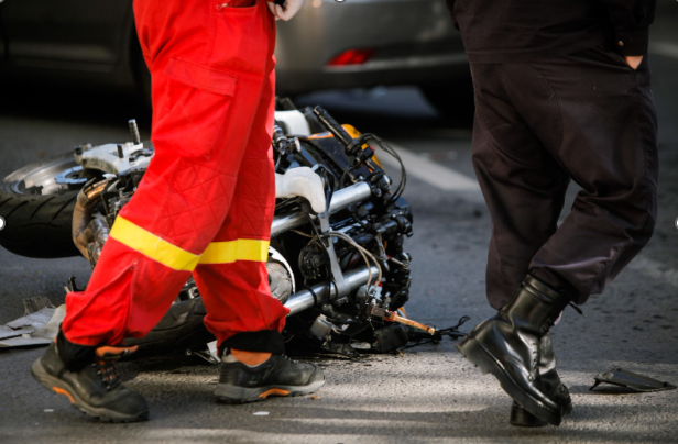Emergency responder and police officer standing beside a motorcycle wrecked on the road after a crash in Western New York